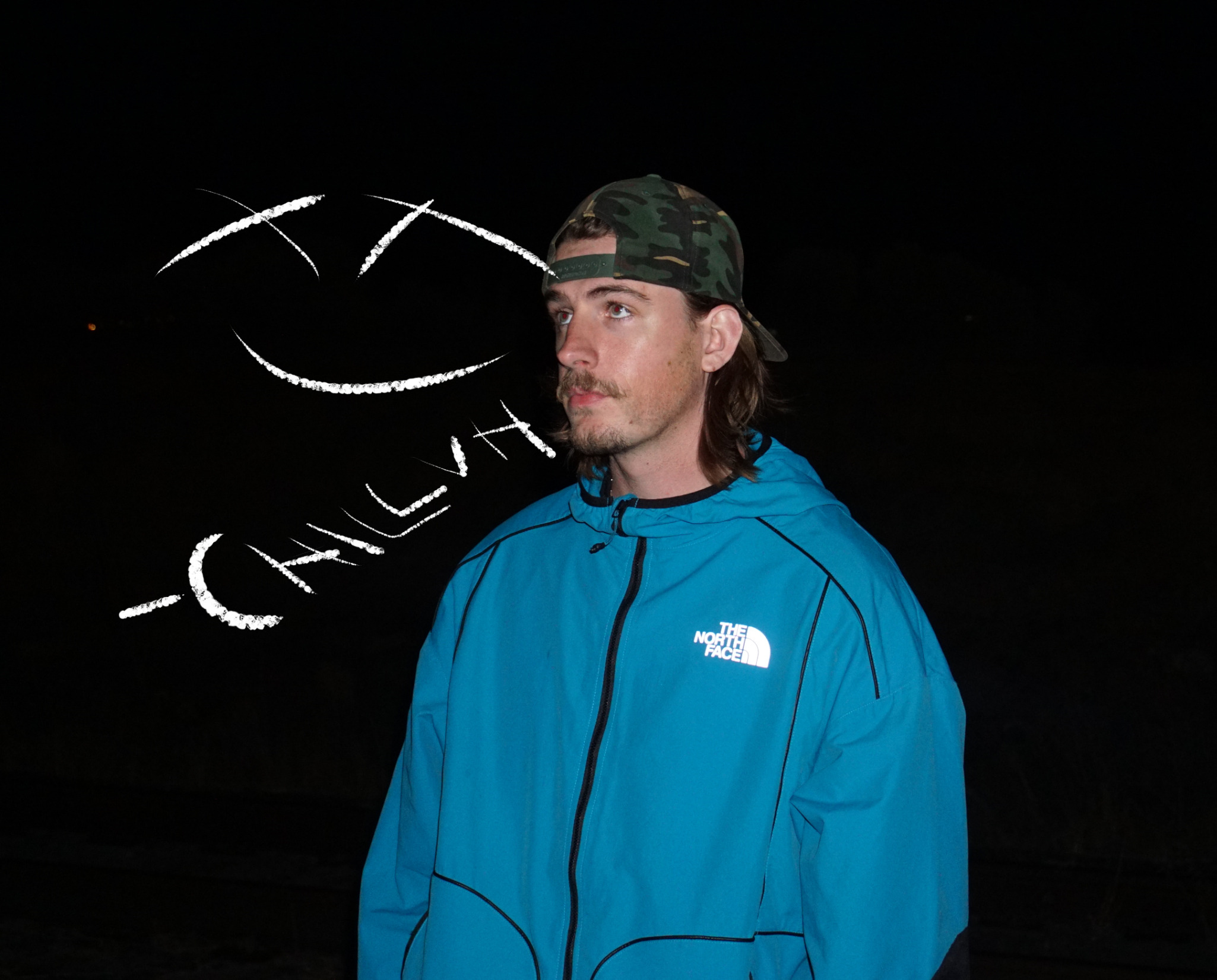 CHILLVH in a blue jacket and camo cap against a dark backdrop with his logo drawn in light